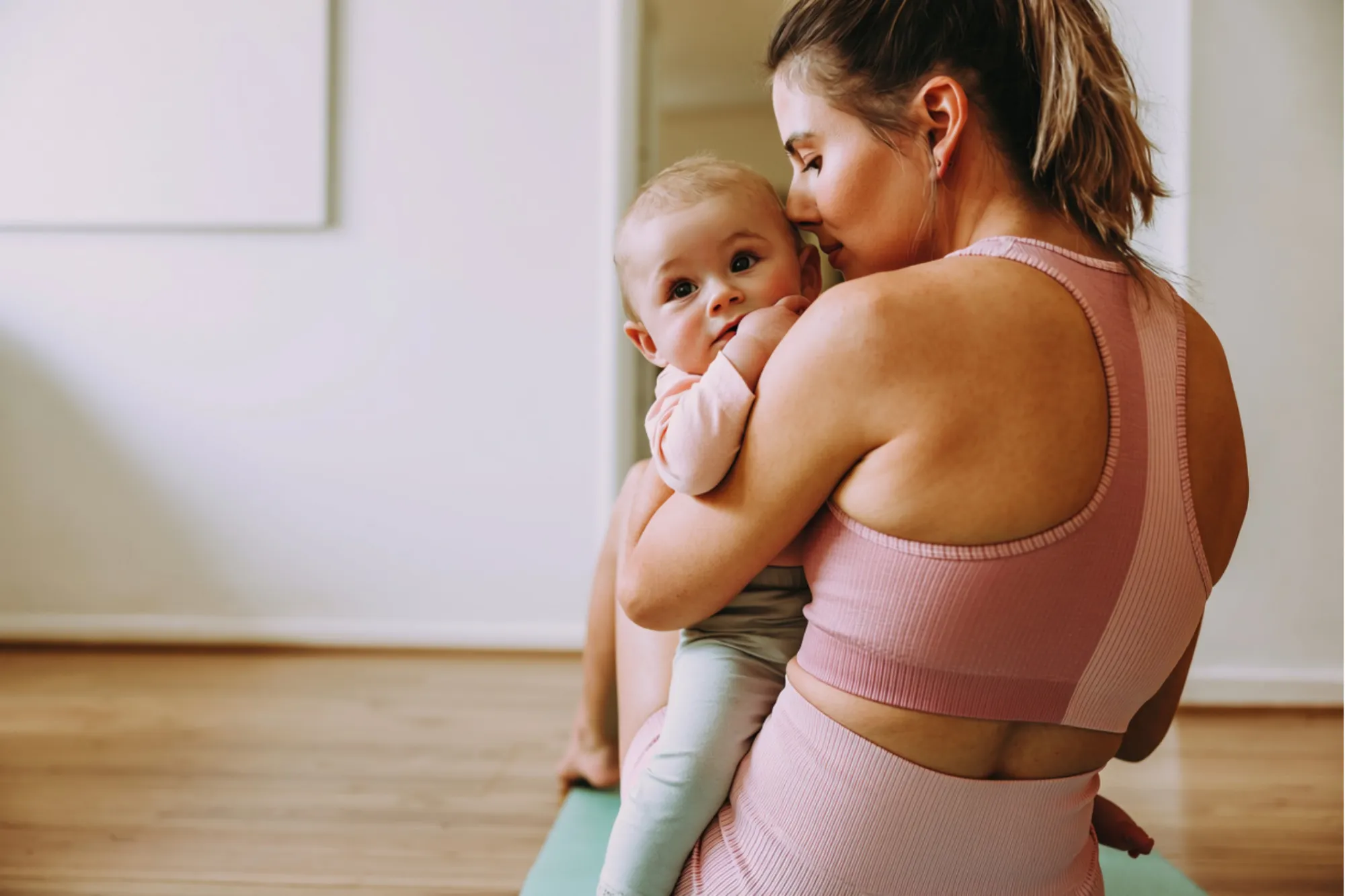 Mom in pink workout clothes holding her baby on an exercise mat