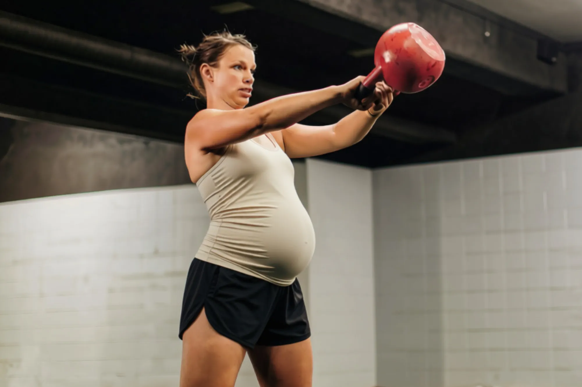 Pregnant woman swinging a red kettlebell to chest height in a gym